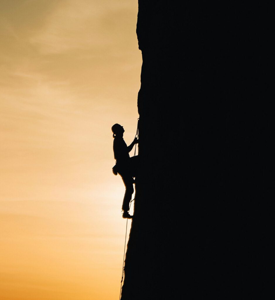 Ein Bergsteiger erklimmt einen steilen Berg, symbolisch für die Herausforderungen im SEO und Online-Marketing, denen sich Bauheld zu Beginn der Zusammenarbeit stellte, um langfristig den Gipfel der digitalen Sichtbarkeit und Performance zu erreichen.
